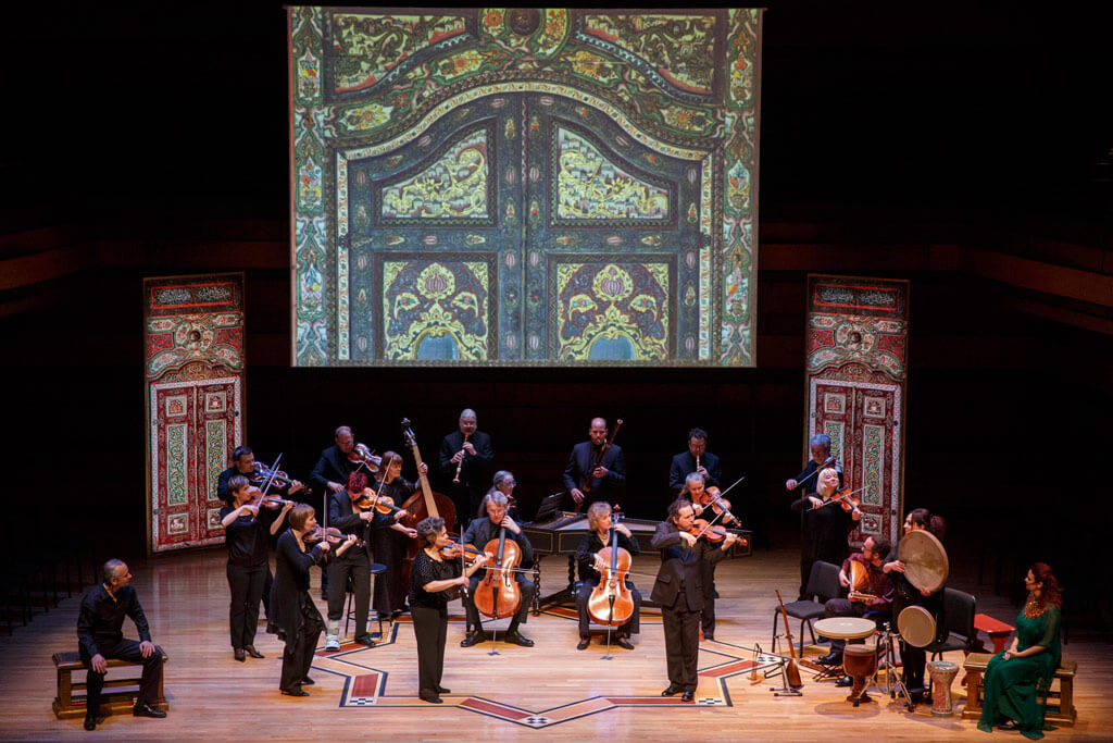 Tafelmusik: “Tales of Two Cities: The Leipzig-Damascus Coffee House.” L-R: Actor Alon Nashman (seated); Tafelmusik Baroque Orchestra (standing); Trio Arabica (lower right). (Photo: Bruce Zinger)