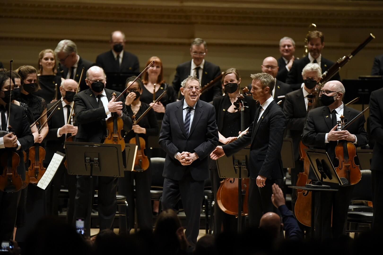Philip Glass recevant les applaudissements du public et de l'orchestre lors de la première américaine de sa Symphonie no 13 donnée par l'Orchestre de CNA et Alexander Shelley au Carnegie Hall (Phot0 : Dominick Mastrangelo)