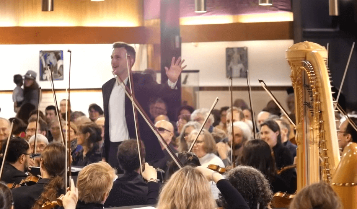 Andrei Feher surpris par les cloches de l'église St-Marcel alors qu'il vient de donner le dernier accord de la symphonie. (Photo : capture d'écran de la vidéo disponible sur le Facebook de l'orchestre Ondes Plurielles)