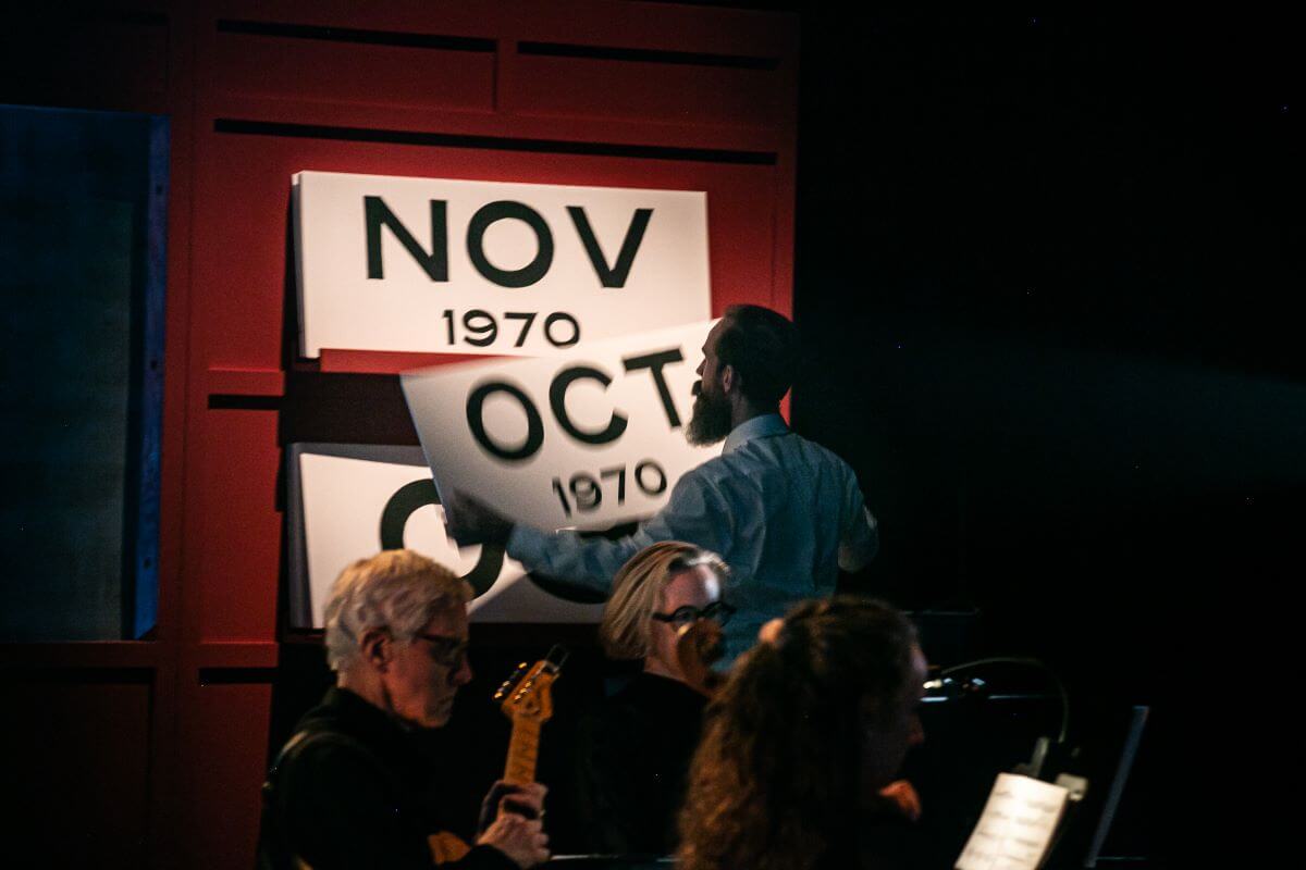 En avant-plan, une partie de l'ensemble instrumental : Tim Brady (guitare électrique et composition), Pamela Reimer (piano) et Chloé Dominguez (violoncelle), tandis que Clayton Kennedy change la page du calendrier. (Photo : Pierre-Étienne Bergeron)