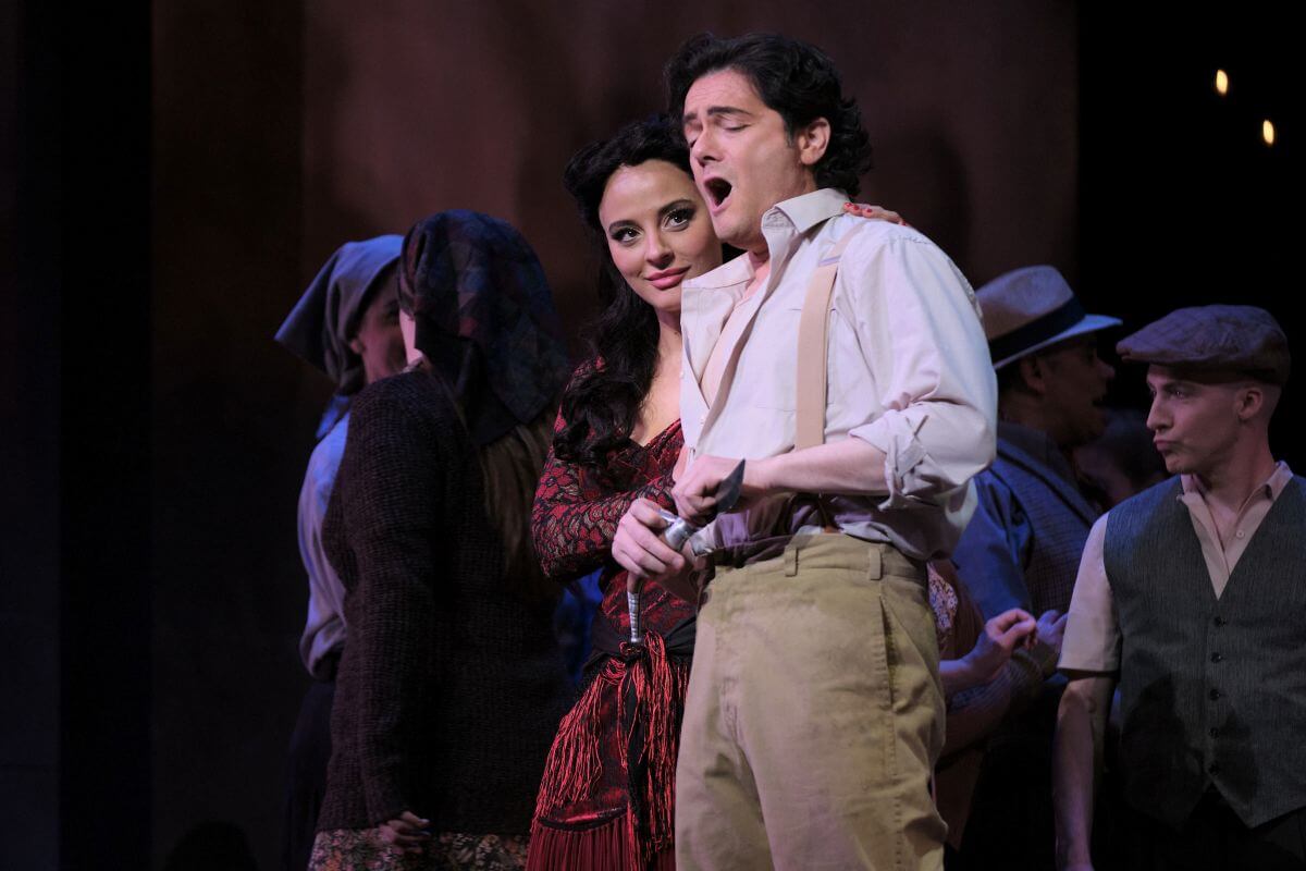 Carmen (Rihab Chaieb), le regard tourné vers le visage de Don José (Arturo Chacón-Cruz) qui chante en affûtant un couteau. (Photo : Vivien Gaumand)