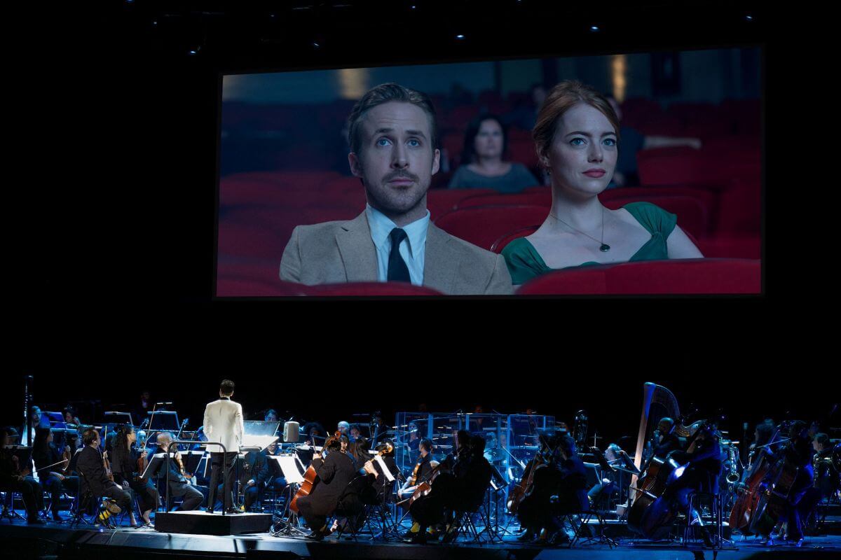 Orchestre sur scène accompagnant le film La la land, dont on voit sur un écran au-dessus de la scène les vedettes Ryan Gosling et Emma Stone assis côte à côte. (Photo : courtoisie)