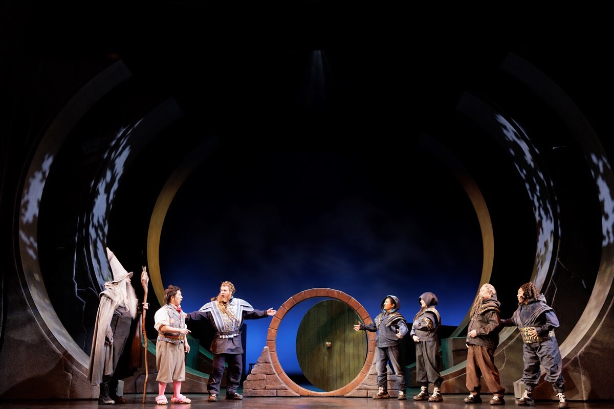 Members of the company, The Hobbit. Stratford Festival 2026 (Photo: David Hou) Ensemble performers stand onstage around a round doorway set.
